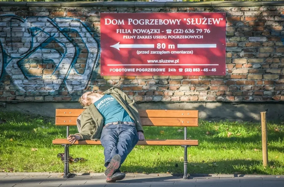 Person slumped on a bench beneath a funeral home billboard